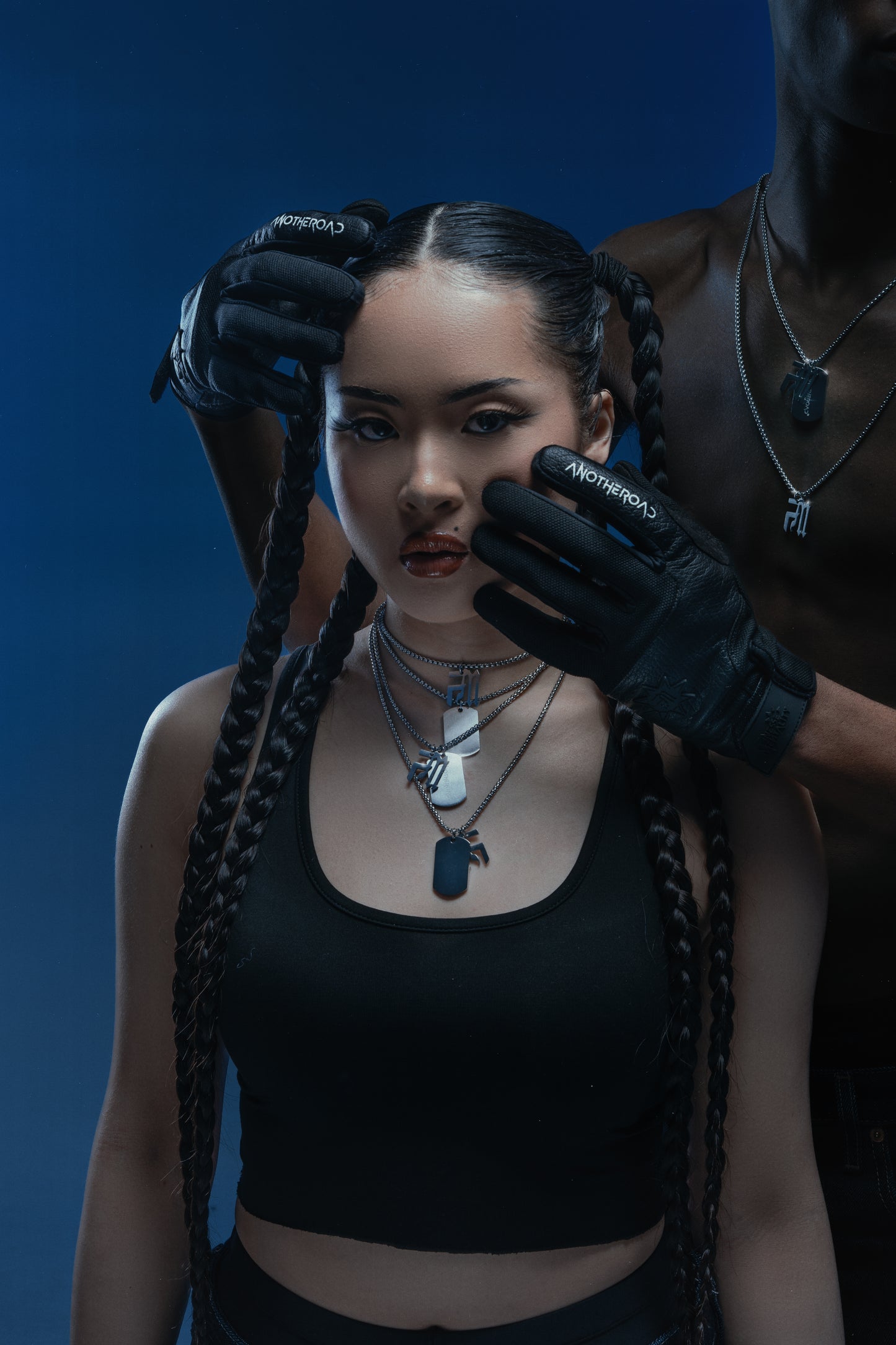 Femme en crop top noir portant quatre chaînes Finesse, coiffée de tresses, touchée au visage par un homme torse nu aux gants Finesse et chaînes 2.