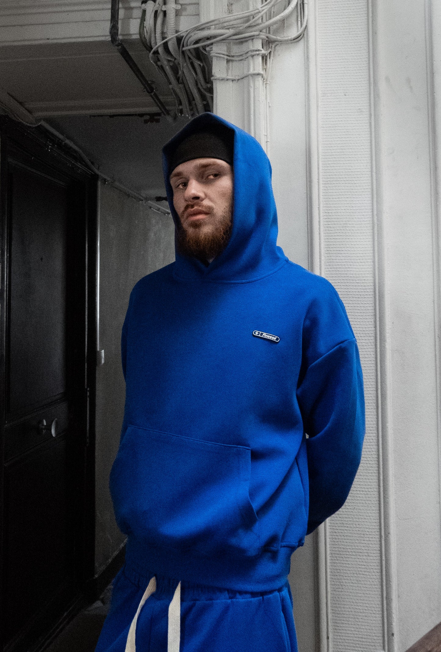 Homme barbu en bonnet portant le Finesse Air Cotton Hoodie bleu, regard pensif dans un bâtiment.