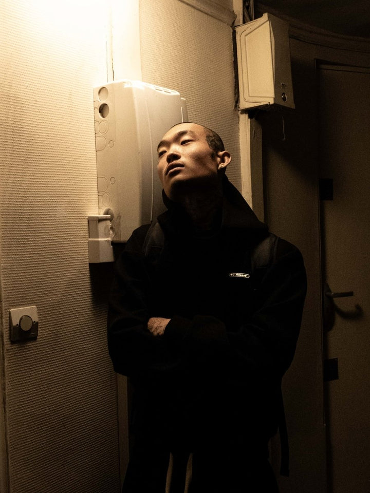 Homme en Finesse Air Cotton Hoodie noir, capuche relevée, yeux fermés près d’un compteur électrique.