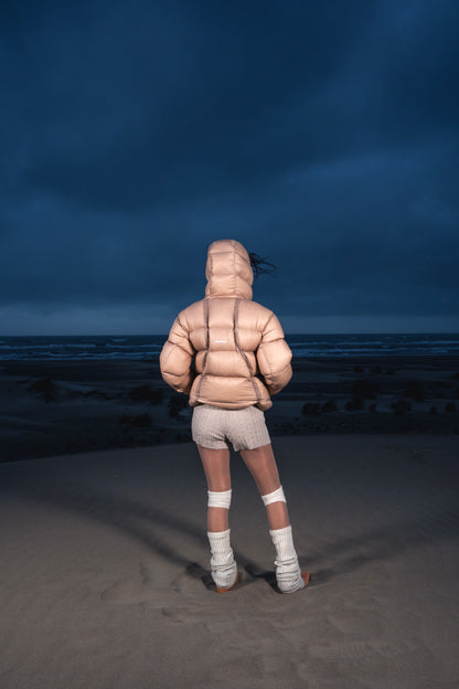 Femme de dos dans les dunes portant la Finesse Alive Puffer Jacket beige