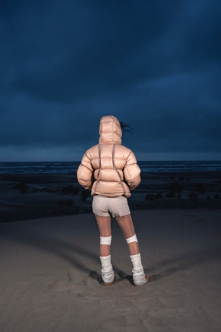 Femme de dos dans les dunes portant la Finesse Alive Puffer Jacket beige