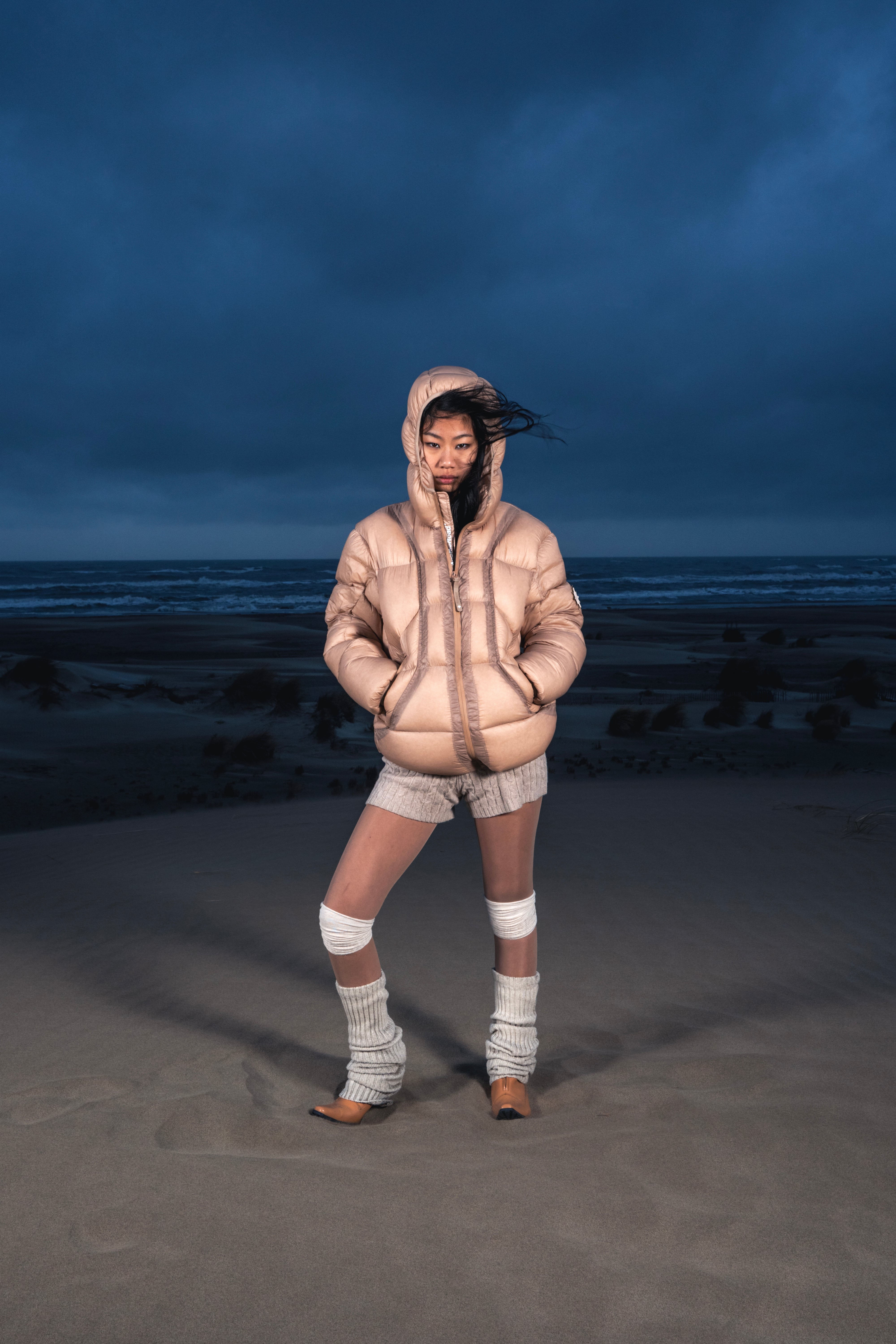 Femme de face dans les dunes portant la Finesse Alive Puffer Jacket beige.
