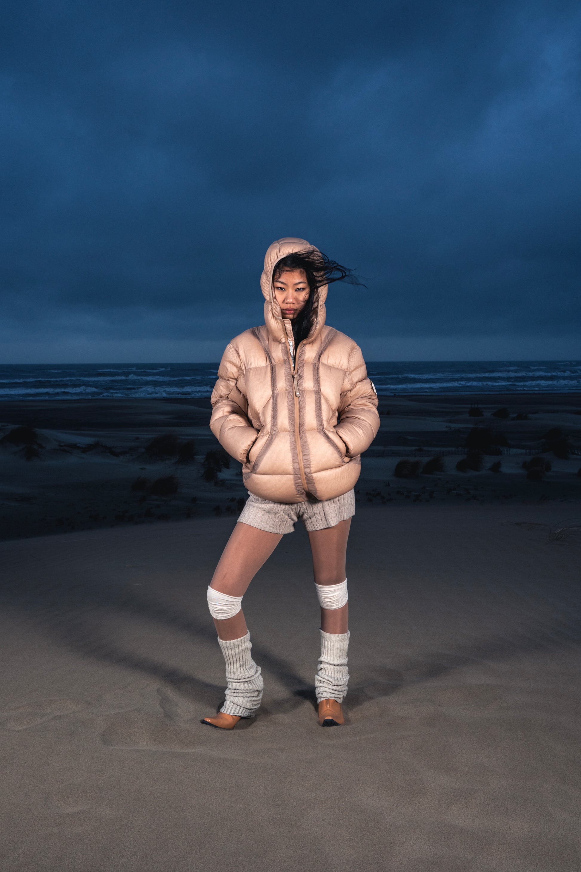 Femme de face dans les dunes portant la Finesse Alive Puffer Jacket beige.
