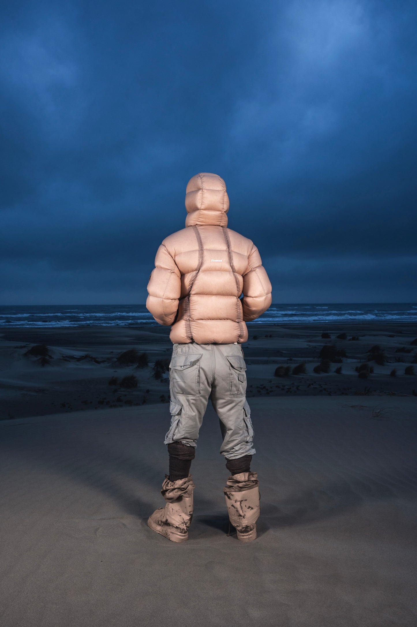 Homme de dos dans les dunes au crépuscule en Alive Puffer Jacket beige