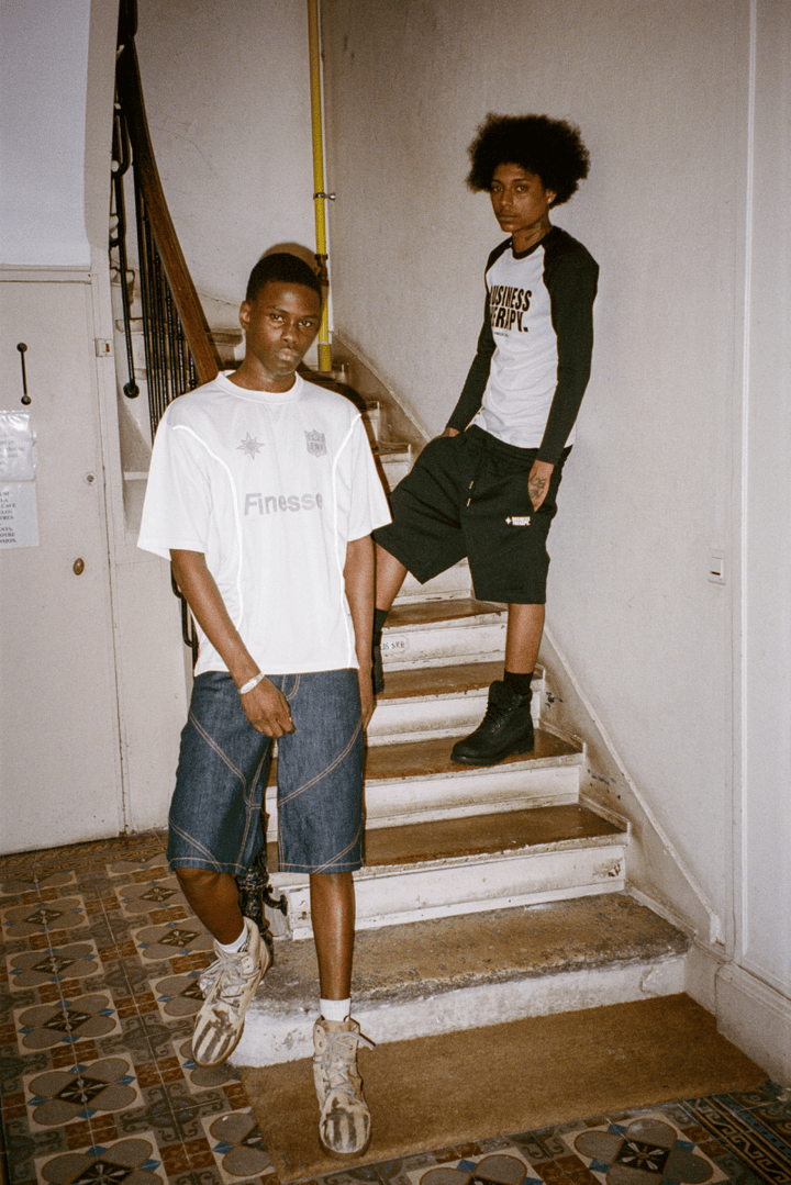 Deux hommes dans une cage d’escalier ancienne, l’un tatoué en Baseball Tee Finesse Business Therapy, l’autre en Jersey Shirt Finesse.