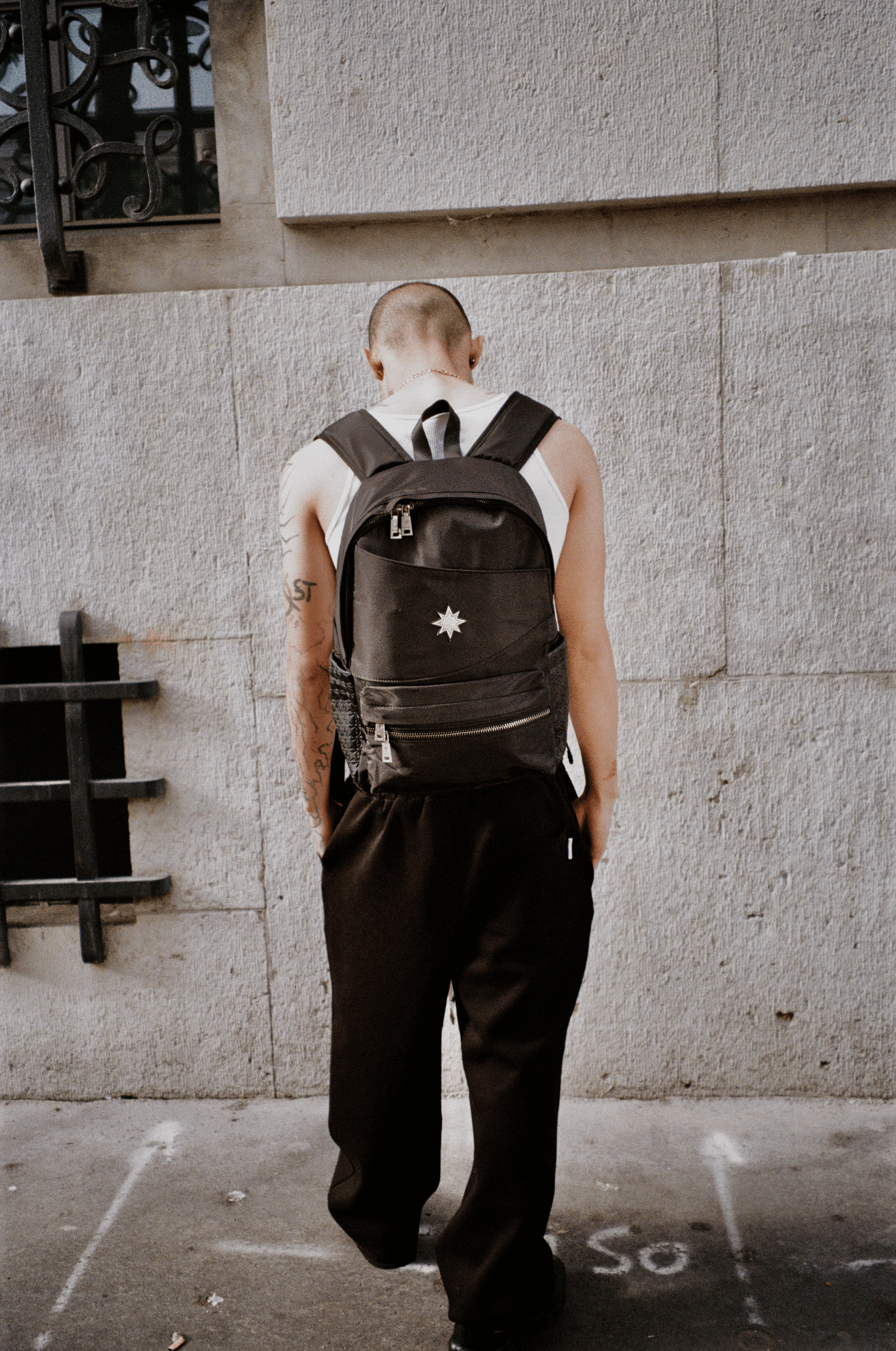 Homme vu de dos devant mur urbain portant le Finesse Black Vanta Backpack.