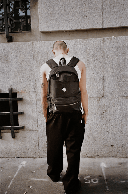 Homme vu de dos devant mur urbain portant le Finesse Black Vanta Backpack.