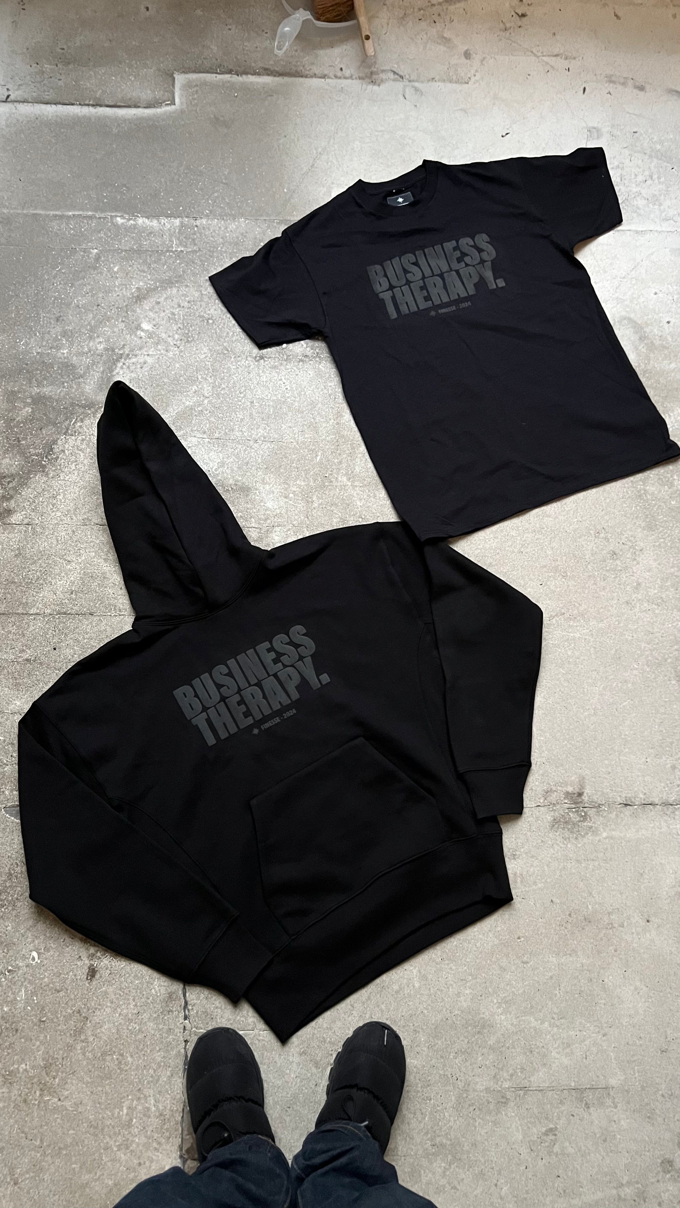 Hoodie et T-shirt Business Therapy Black on Black posés ensemble au sol