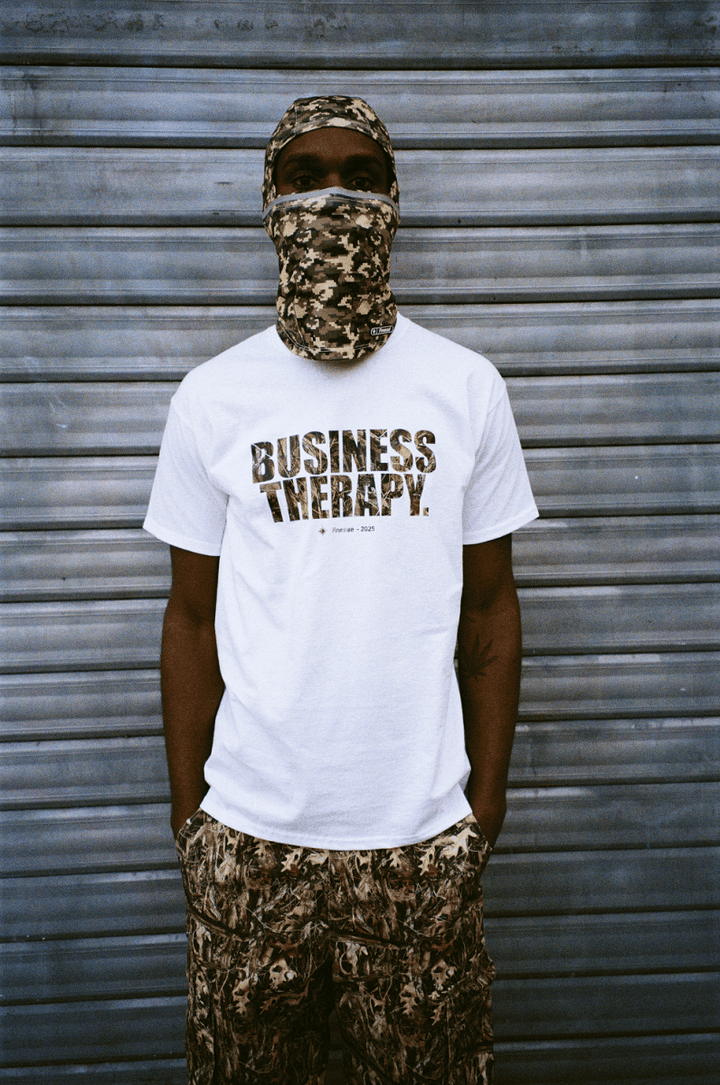 Homme cagoulé devant un rideau de fer, portant le Business Therapy Camo T-shirt, plan resserré sur le torse.