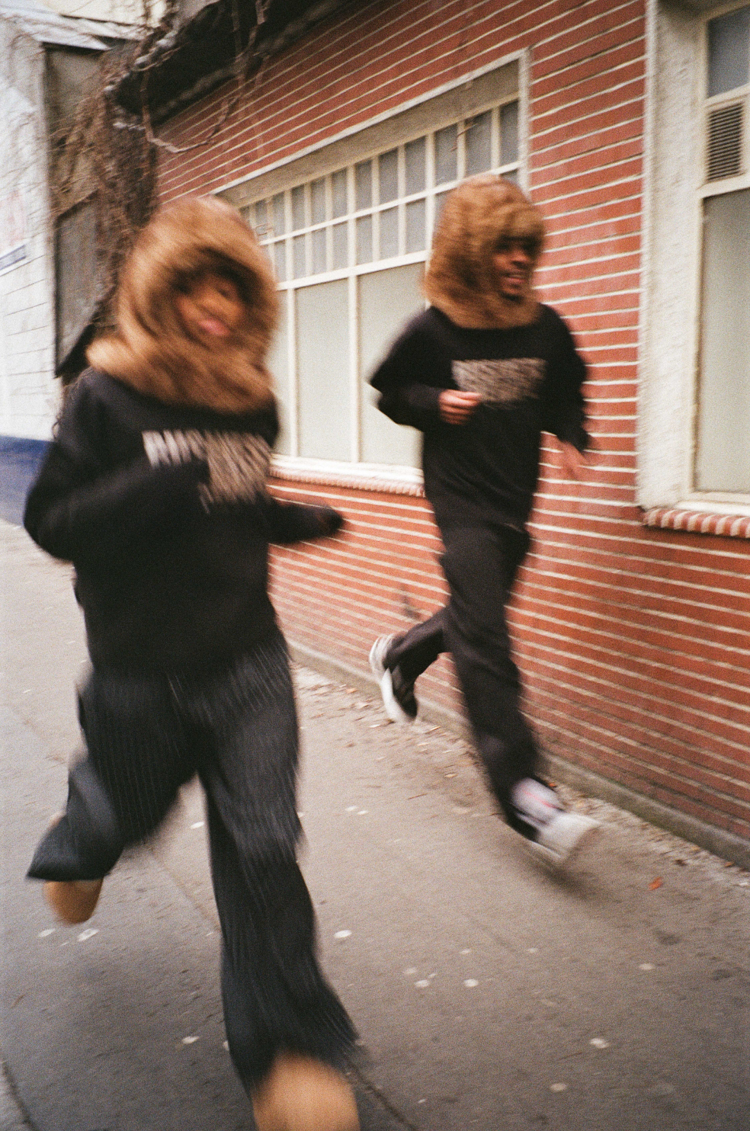 Deux mannequins en mouvement dans un environnement urbain, en Crew Neck FUR et FUR HOOD.