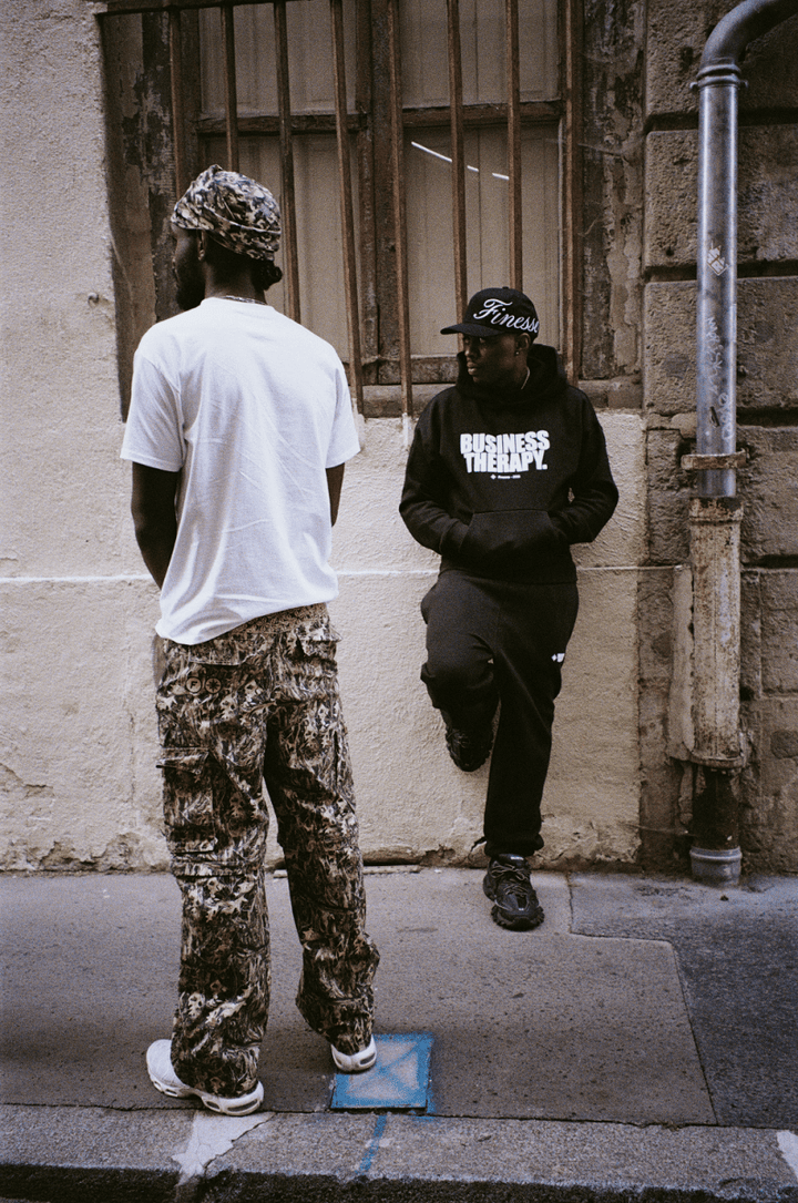 Homme de dos en 2-in-1 Cargo Pants, second mannequin en Business Therapy noir avec Finesse "SIGN" Cap Black.