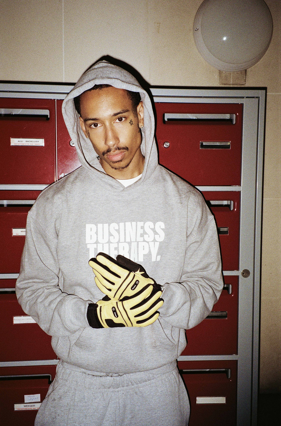 Homme en hoodie Business Therapy gris avec gants Finesse dans cage d’escalier à boîtes rouges.
