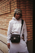 Homme cagoulé en jogging gris Business Therapy, au coin de la rue devant mur de briques