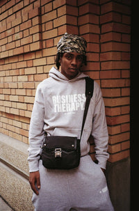 Homme cagoulé en jogging gris Business Therapy, au coin de la rue devant mur de briques