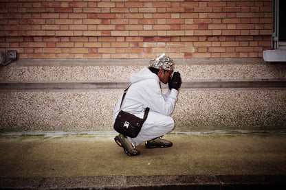 Homme accroupi en jogging gris Business Therapy avec Memorial Bag, mains jointes comme en prière.