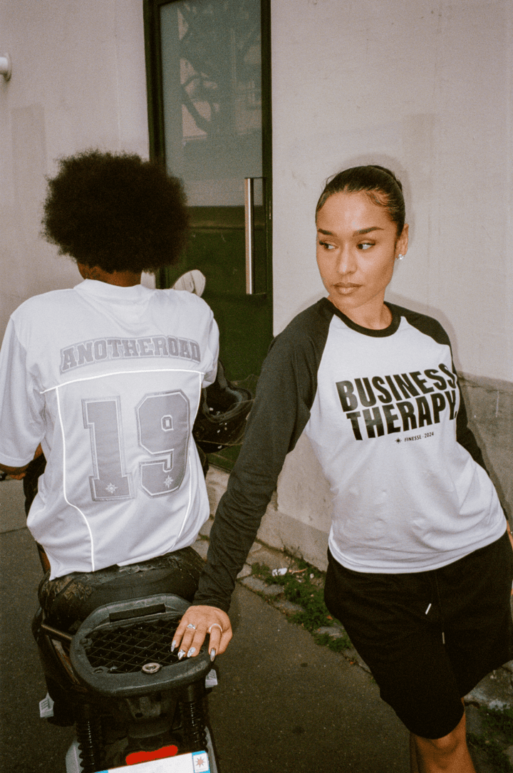 Homme de dos assis sur un scooter en Jersey Finesse, avec une femme de face en Long Sleeve Business Therapy s’appuyant sur le scooter.