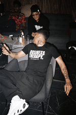 Homme tatoué allongé dans un canapé, portant un t-shirt Business Therapy et des sneakers blanches.