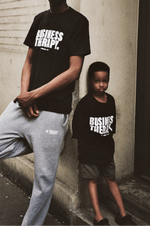 Enfant adossé à un adulte dans un décor urbain, tous deux portant un t-shirt Business Therapy.