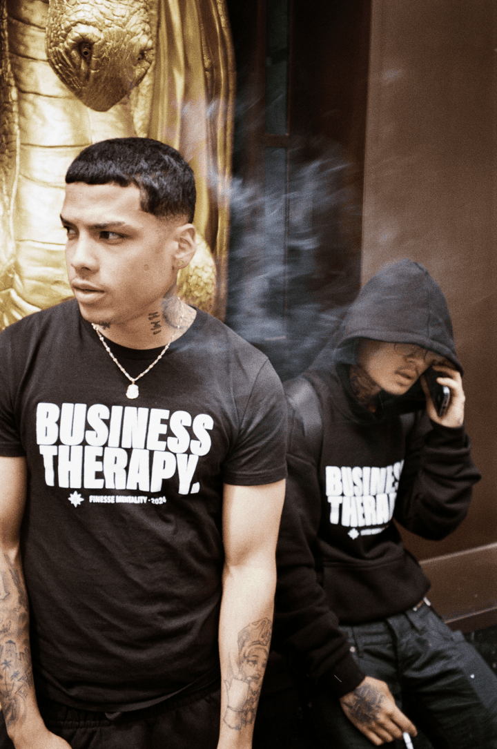 Deux hommes en milieu urbain regardant la caméra, vêtus de t-shirts Business Therapy.