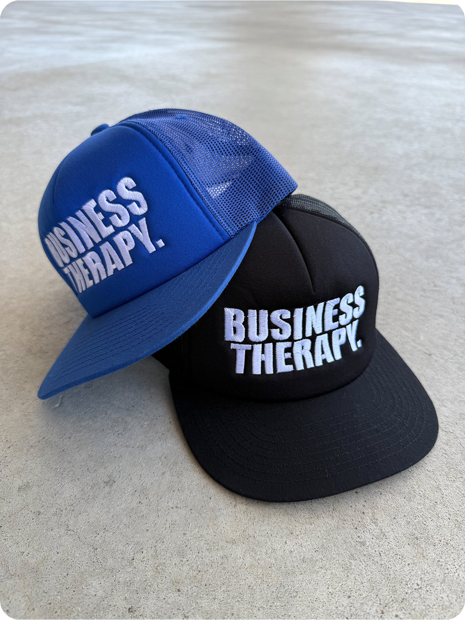 Packshot au sol de deux casquettes Business Therapy Trucker, coloris bleu et noir