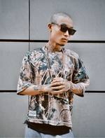 Homme tatoué en Jersey 44 camo, lunettes Sunglasses Series 01, mains jointes.