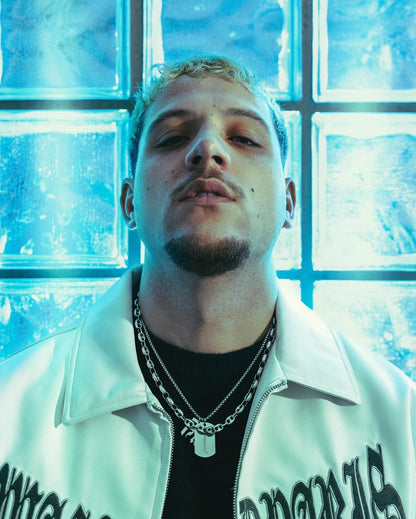 Homme de buste portant la chaîne Finesse et une veste blanche, posé devant un fond à carreaux éclairé de lumière bleue.