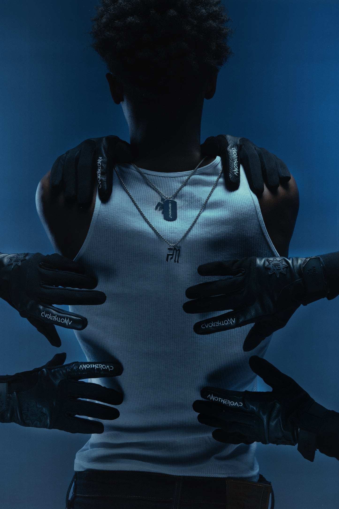 Homme en débardeur blanc vu de dos en studio, portant deux chaînes Finesse et gants Finest as a Gloves, entouré de mains gantées.