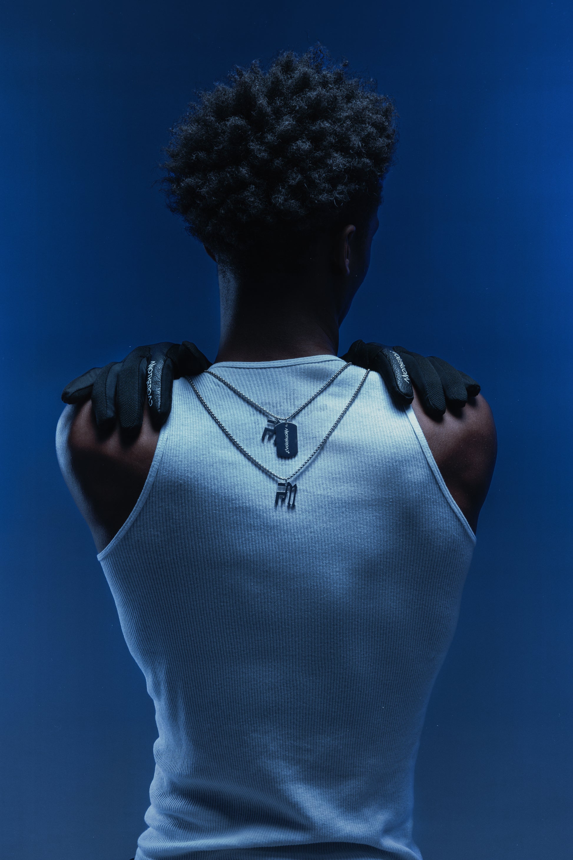 Photo de dos d’un homme en débardeur blanc portant des gants Finesse et deux chaînes Finesse mises en évidence.