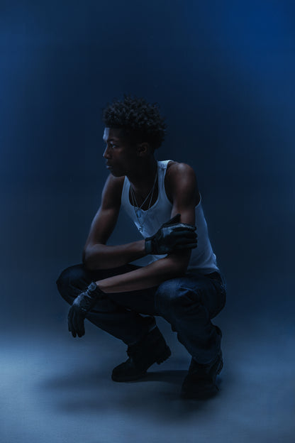 Homme accroupi en studio portant un débardeur blanc et les gants Finesse To The Gloves.