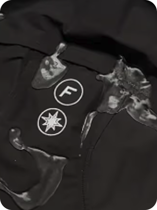 Zoom sur capuche de la FAS Hardshell noire avec gouttes d’eau, montrant son effet déperlant.