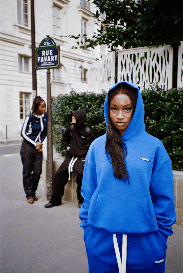 Scène rue Favard à Paris : trois personnes, femme en avant-plan avec capuche portant l’ensemble Air Cotton bleu."