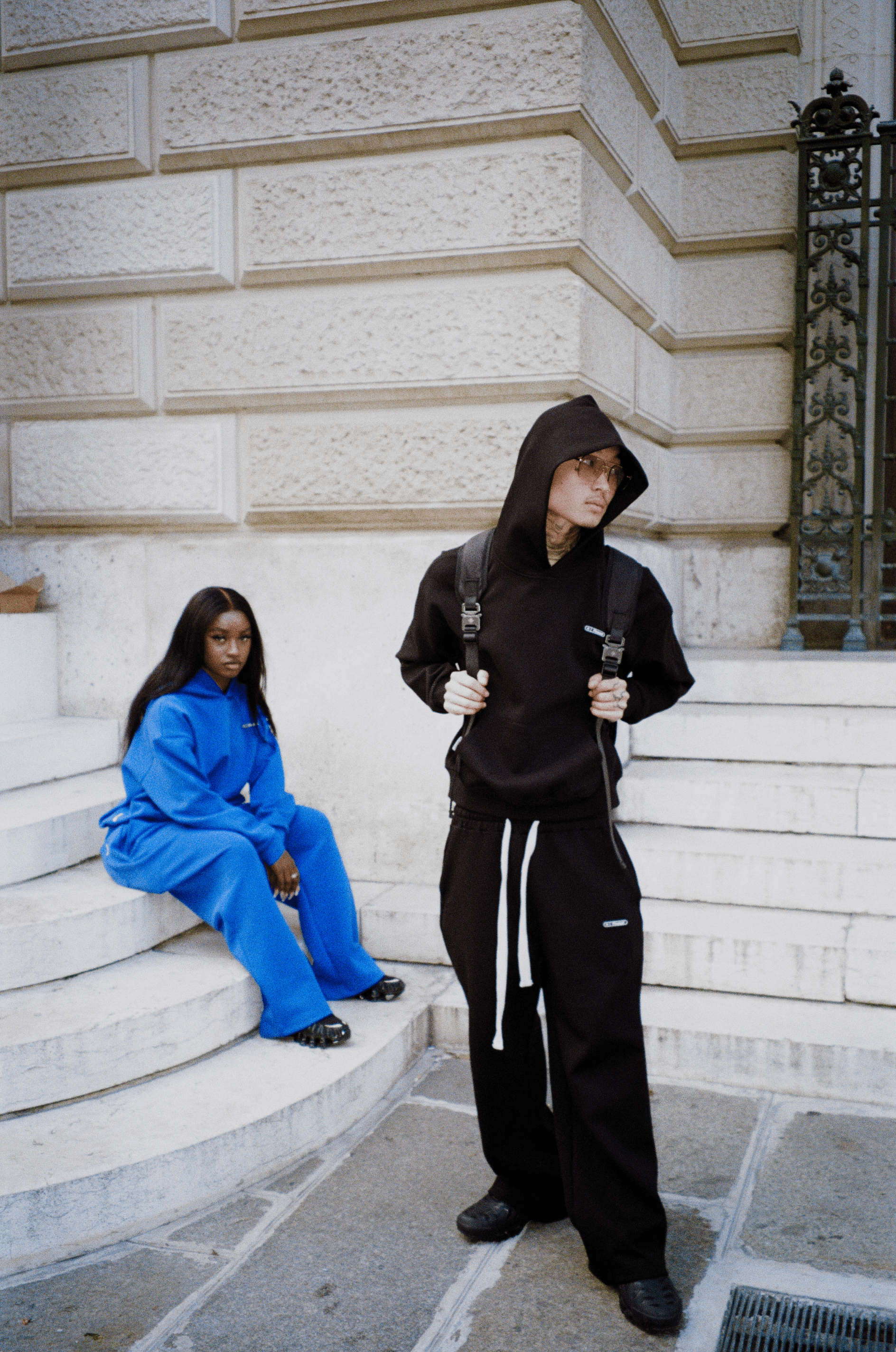 Deux mannequins : femme assise en arrière-plan en ensemble Air Cotton bleu, homme en avant-plan en ensemble noir.