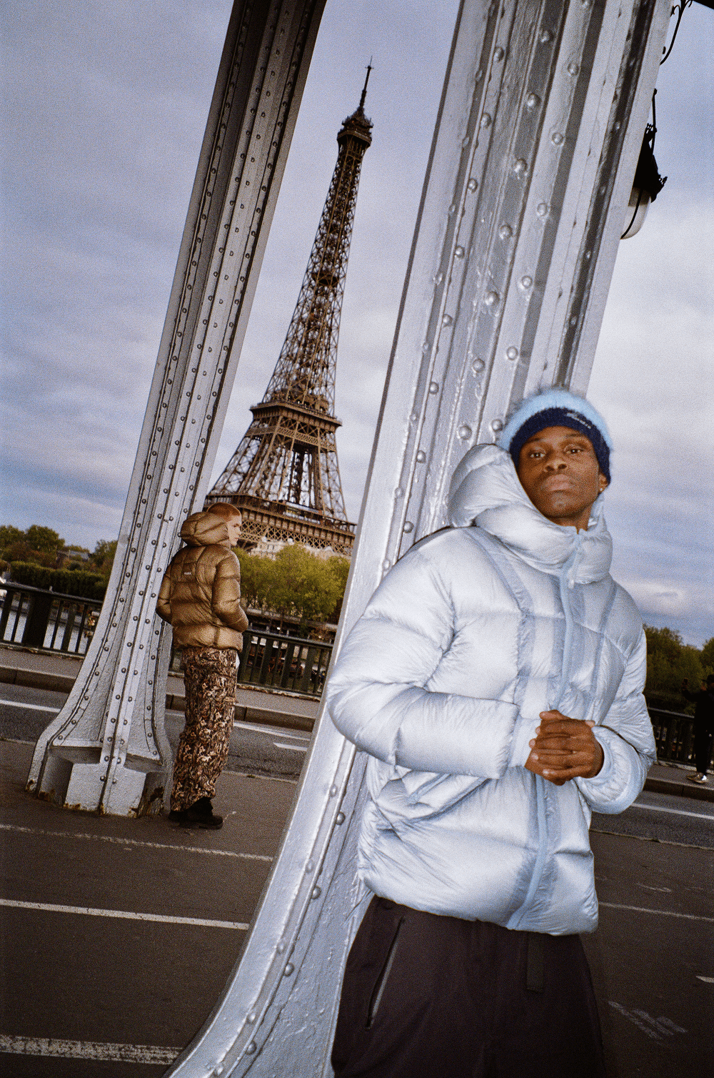 Photo argentique d’un homme portant la Finesse* Alive Puffer Jacket Ice Blue sur un pont à Paris.