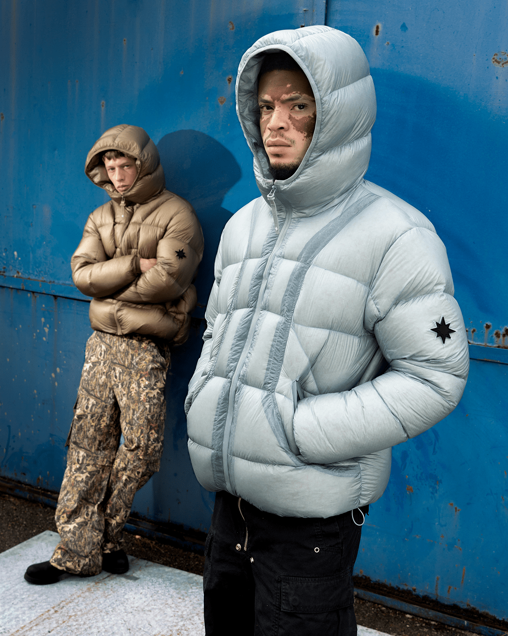 Deux mannequins portant les doudounes Finesse* Alive Puffer Jacket Ice Blue et Light Bronze devant un mur bleu.