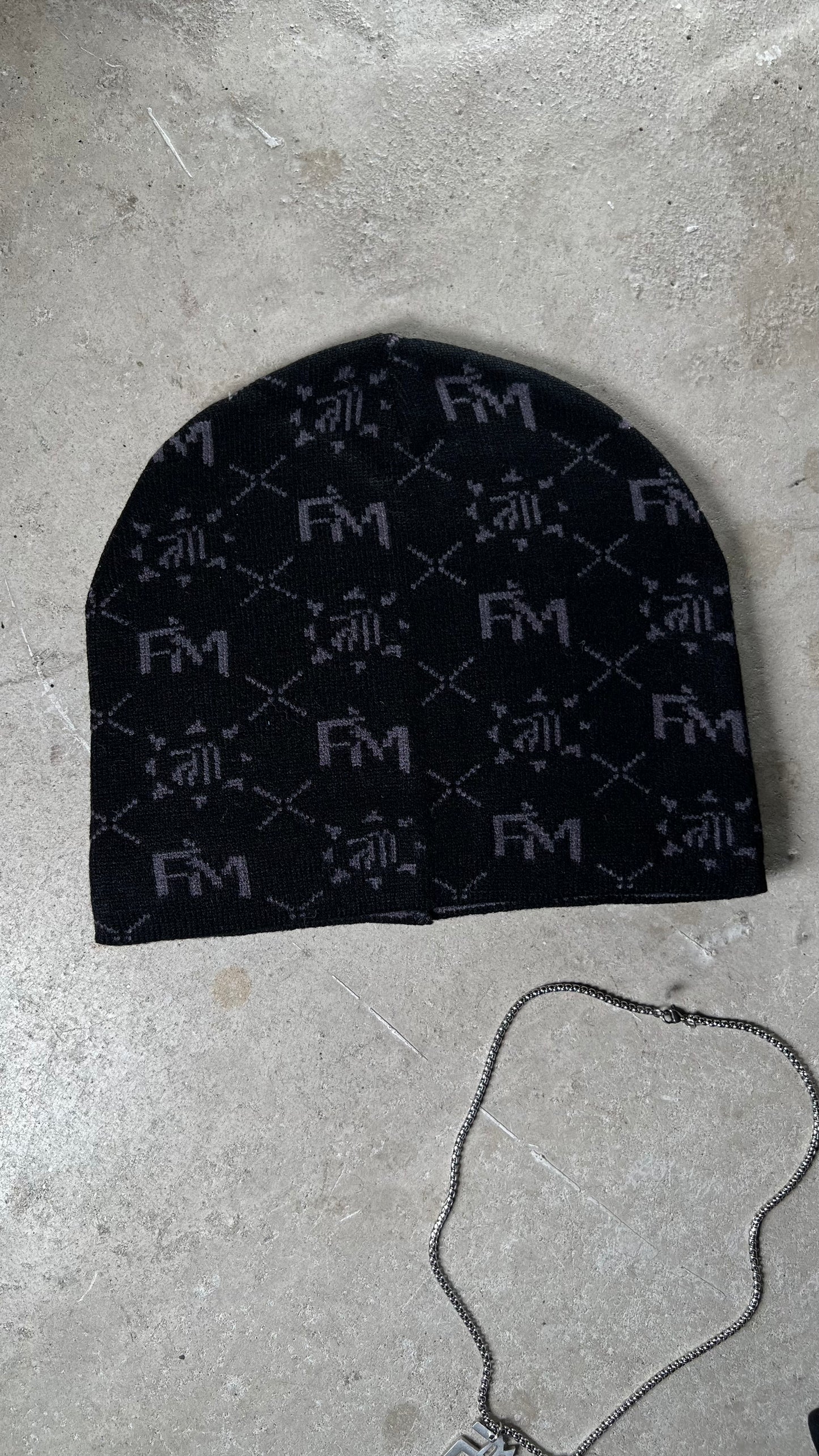 Bonnet Finesse Black Earth avec la chaîne FM Necklace en packshot sur fond blanc.