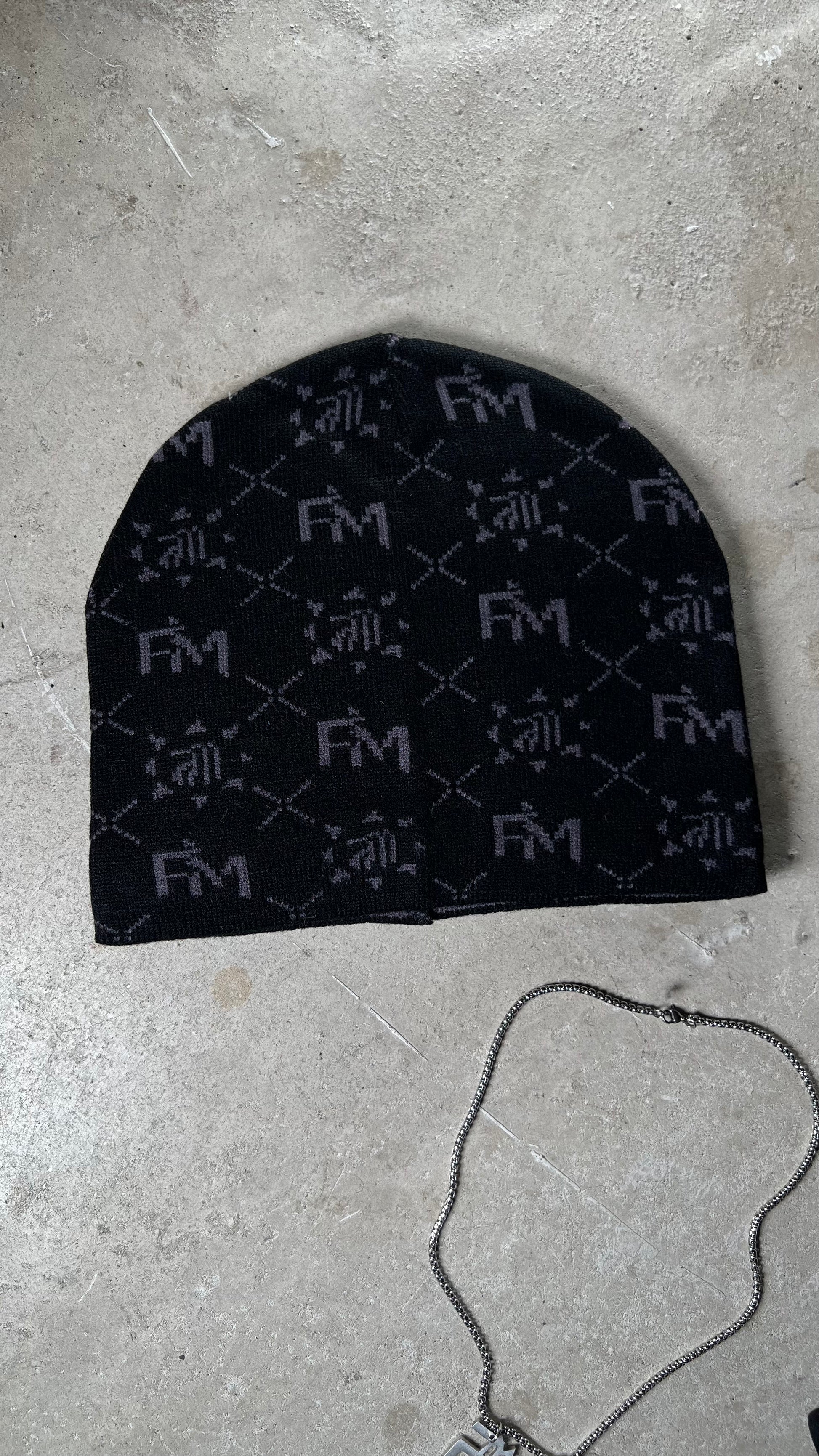 Bonnet Finesse Black Earth avec la chaîne FM Necklace en packshot sur fond blanc.