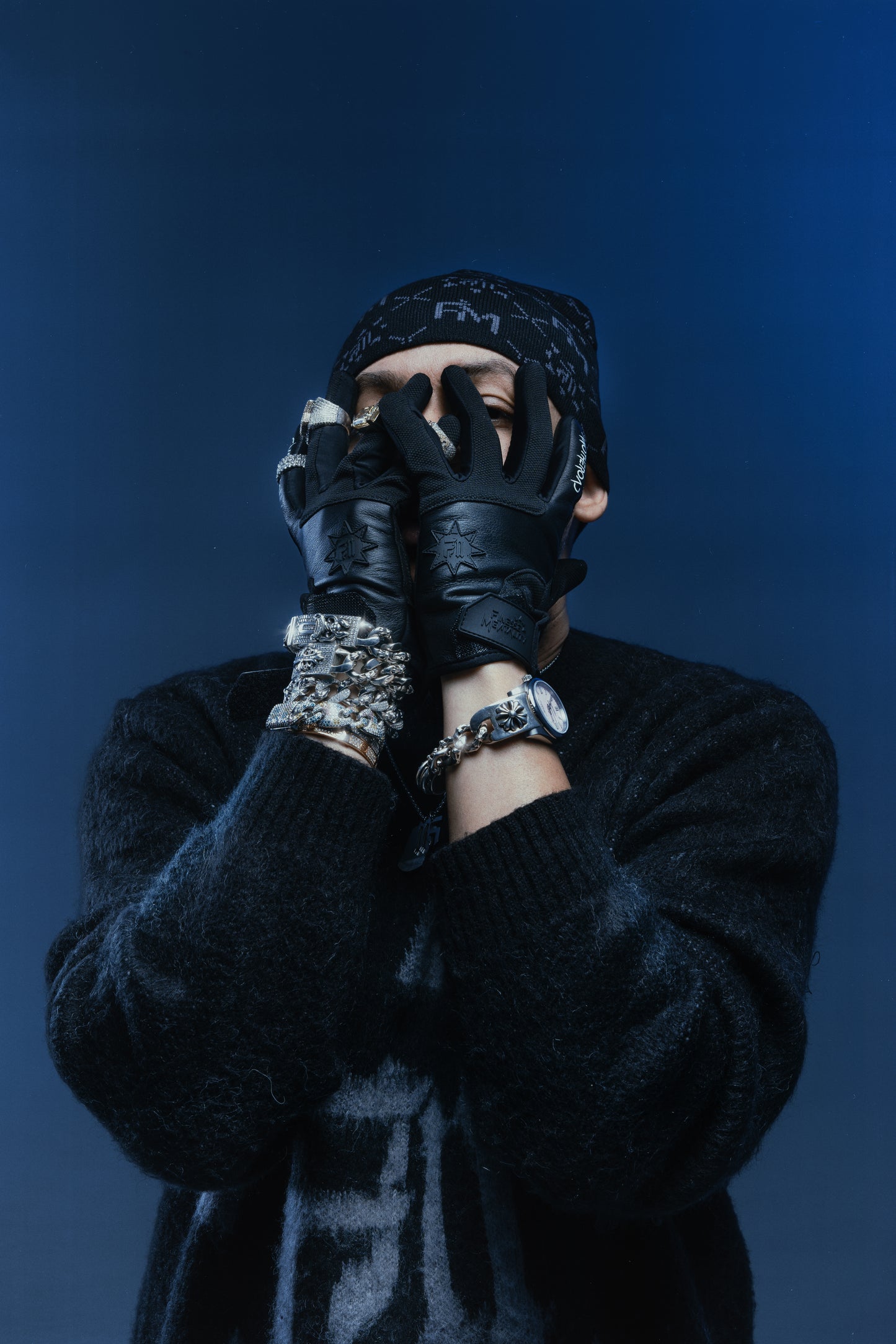 Homme en studio sur fond bleuté avec bonnet Finesse Black Earth, gants Finest Gloves et knit Mohair noir, bijoux diamantés.