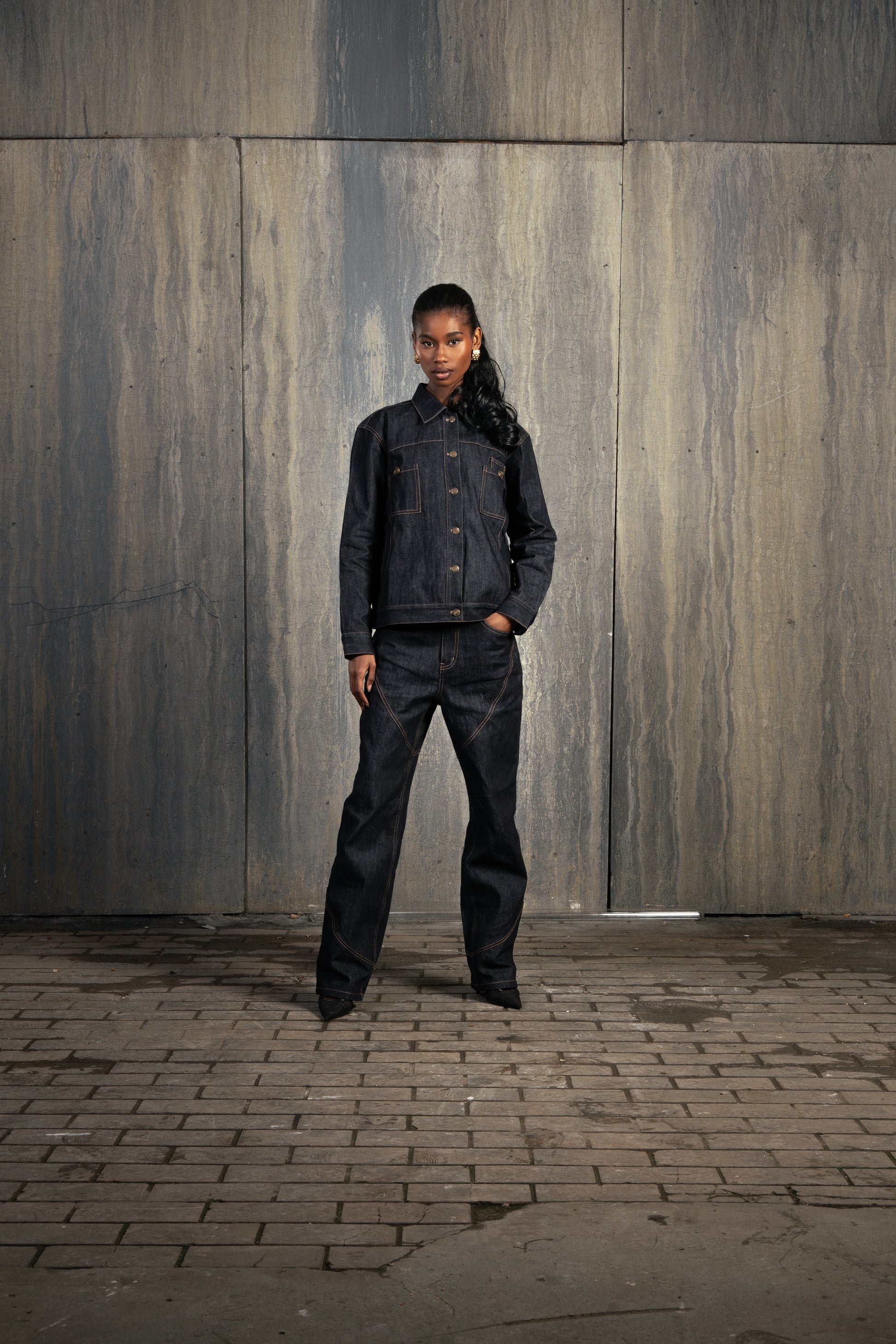 Femme autre de face en studio décor industriel, main dans la poche, portant le Finesse Denim Set ADV avec allure affirmée.