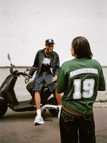 Plan large avec une femme en Jersey Shirt vert Finesse et un homme riant sur un scooter en Denim Vest Finesse.