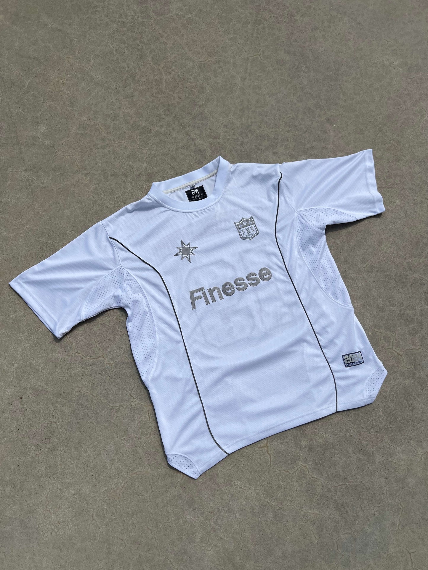 Finesse Jersey Shirt blanc présenté à plat sur sol en béton, vu de face avec logo Finesse.