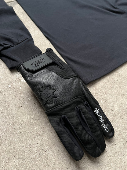 Packshot gros plan sur sol en béton d’un gant Finesse Leather Gloves en cuir, avec un long-sleeve flou en arrière-plan.