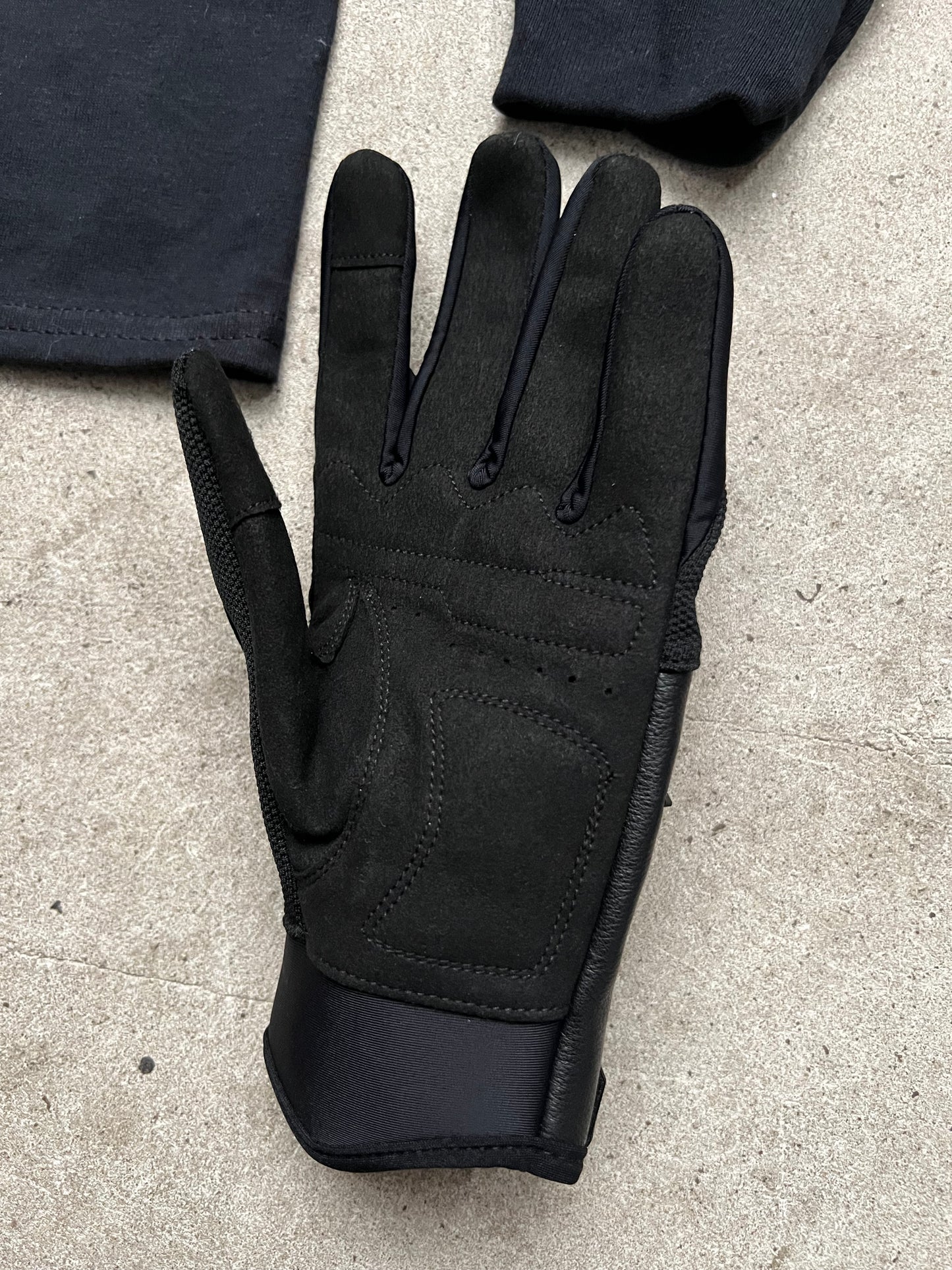 Packshot gros plan sur sol en béton d’un gant Finesse Leather Gloves en cuir, avec un long-sleeve flou en arrière-plan 2.