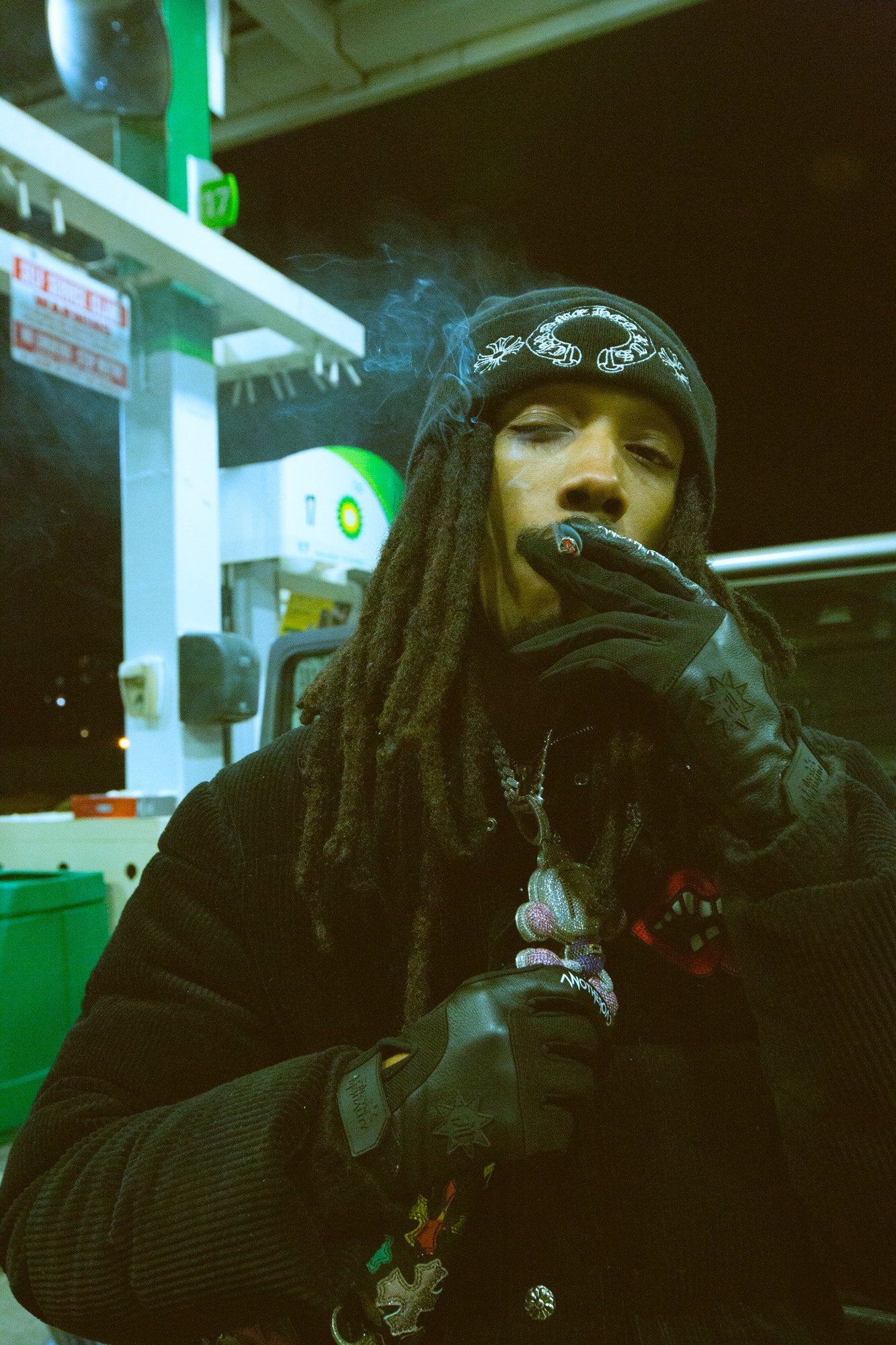 Homme aux dreadlocks dans une station-service, en pull et bonnet noirs, portant les gants Finesse Leather Gloves.
