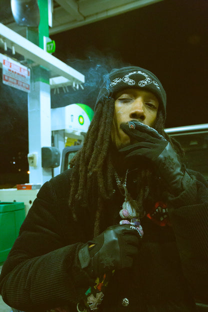 Homme aux dreadlocks dans une station-service, en pull et bonnet noirs, portant les gants Finesse Leather Gloves.
