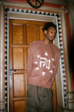 Homme en pantalon kaki portant le Finesse Mohair Brown Bird, posé dans l’encadrement d’une porte en bois.