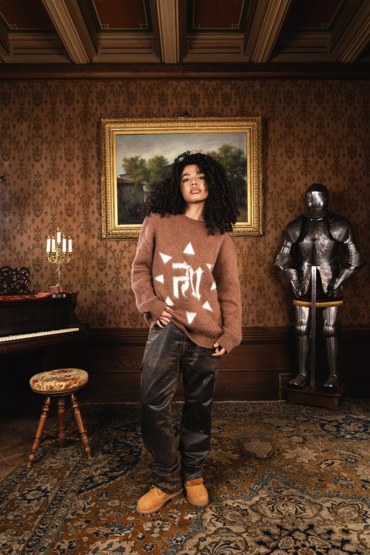 Femme debout avec assurance dans un château, sur moquette ancienne, devant une armure, portant le Finesse Mohair Brown Bird.