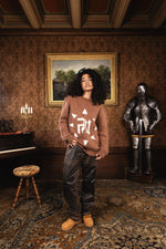 Femme debout avec assurance dans un château, sur moquette ancienne, devant une armure, portant le Finesse Mohair Brown Bird.