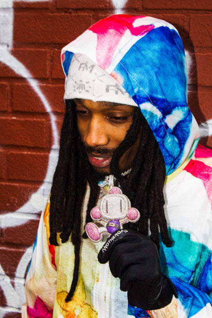 Homme portant le bonnet Finesse Snow et gants Finesse Leather Goat, avec chaîne diamant et sweat multicolore devant un mur de briques.