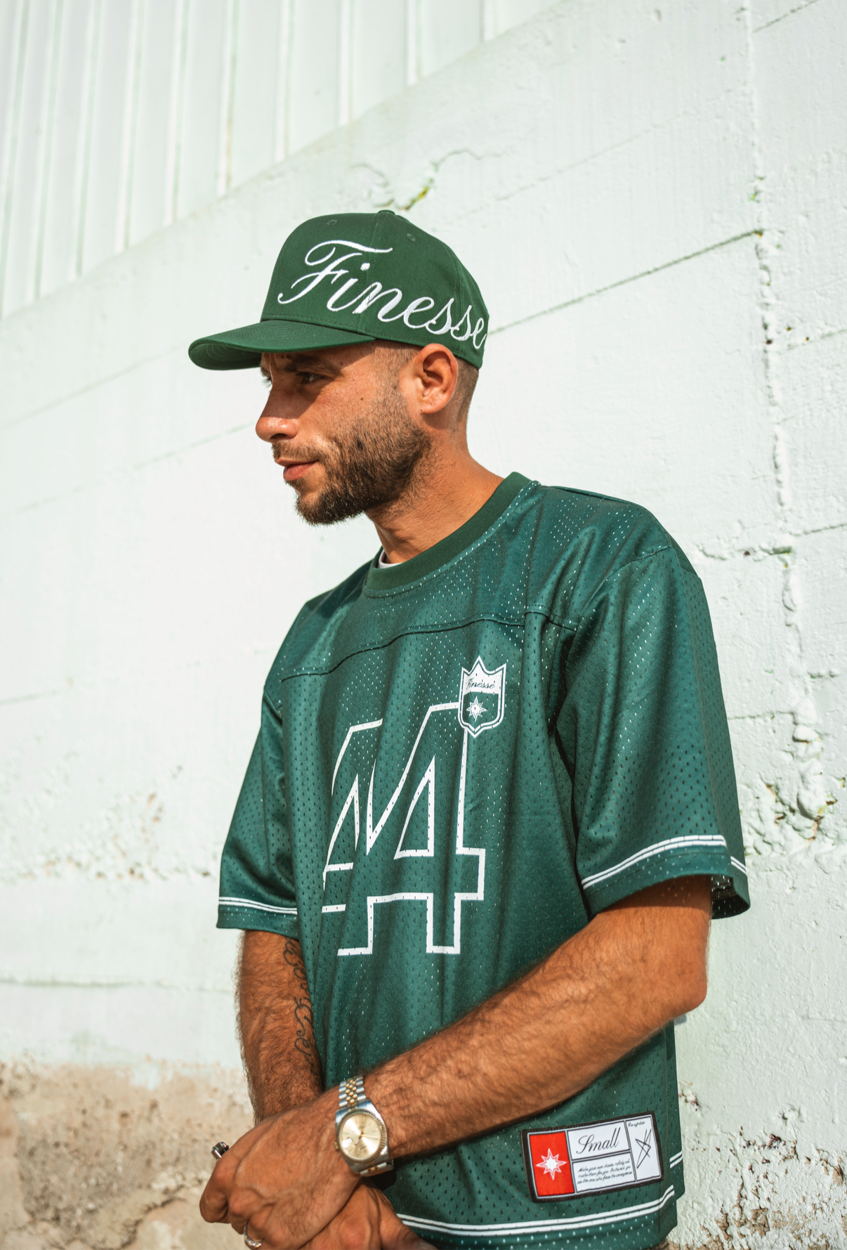 Homme en Jersey 44 green et Sign Cap, adossé à un mur sableux en lookbook urbain