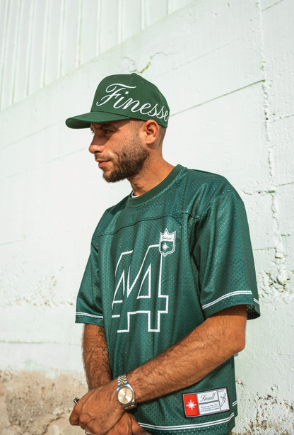 Homme en Jersey 44 green et Sign Cap, adossé à un mur sableux en lookbook urbain
